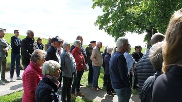 Gäste der Veranstaltung stehen auf einem kleinen Weg und einem Rasenstück. Sie schauen nach rechts.