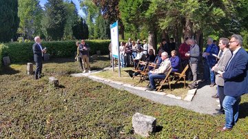 Links ein Mann der spricht. Rechts die Zuhörer um die Geschichts- und Erinnerungstafel