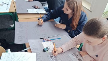 Zwei Schülerinnen schreiben etwas auf ihre Ausstellungsplakate