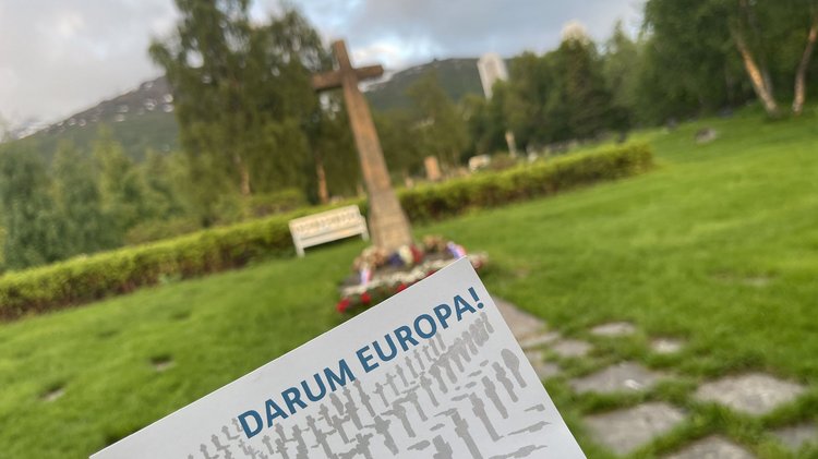 Die Postkarte „Darum Europa“ vor einen Kriegsdenkmal