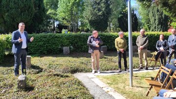 Links ein Mann der beim Sprechen mit den Händen gestikuliert. Rechts zuhörende Menschen.