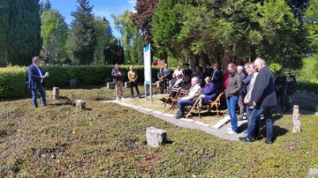 Links im Bild der Bürgermeister der von einem Blatt Papier abliest. Rechts Menschen stehend und Sitzend die zuhören.