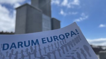 Die Postkarte „Darum Europa“ vor einen Kriegsdenkmal