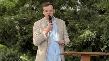 Herr Grünefeld, der Lehrer, hält das Mikrofon in der Hand und spricht zu den Gästen.