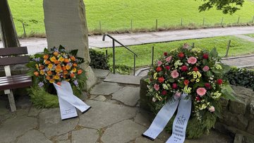 Links ein Kranz der Stadt Leer, angelehnt am Ehrenmal. Auf dem Ehrenmal stehen die Namen der gefallenen Leerorter. Rechts der Kranz des Volksbundes ist an eine Mauer angelehnt. 